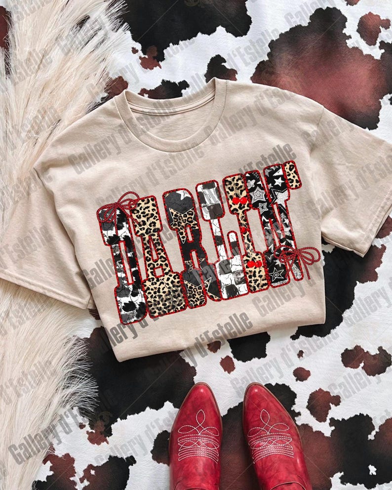 May include: A beige t-shirt with the word "TAKE IT" in a patchwork design featuring cow print, leopard print, stars, and red accents. Red cowboy boots are at the bottom of the image, set against a cowhide pattern.