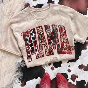 May include: A beige t-shirt with the word "MAMA" in a patchwork design featuring cow print, leopard print, and floral patterns. Red cowboy boots are at the bottom of the image, with a cowhide pattern in the background.