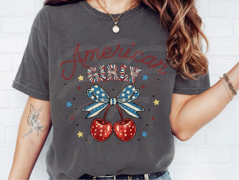 May include: A grey t-shirt with a red, white and blue American flag design. The design features a bow with cherries and the text "American Girl".