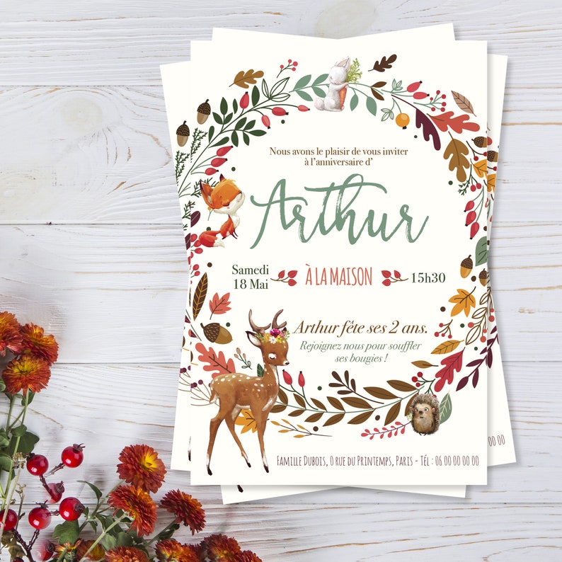 May include: A white invitation card with a woodland theme. The card features a wreath of leaves, flowers, and animals, including a fox, a deer, and a hedgehog. The text on the card reads "Nous avons le plaisir de vous inviter &agrave; l'anniversaire d'Arthur Samedi 18 Mai &Agrave; LA MAISON 15h30 Arthur f&ecirc;te ses 2 ans. Rejoignez nous pour souffler ses bougies! FAMILLE DUBOIS, O RUE DU PRINTEMPS, PARIS-TEL: 06 00 00 00 00 00.00"