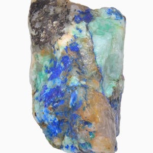 May include: A raw, uncut mineral specimen with a mix of colors. The stone features patches of deep blue, teal, and green, contrasted by areas of tan, gray, and clear crystal. The rough texture and varied hues create a natural, earthy aesthetic.