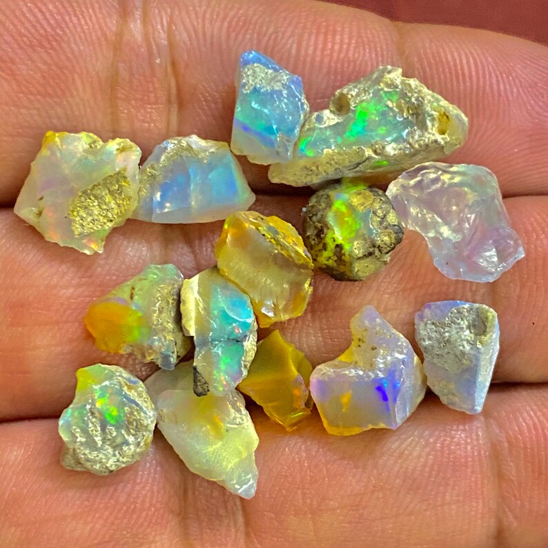 May include: A collection of raw opal gemstones, showcasing a variety of colors including blue, green, yellow, and white. The opals have a rough, natural texture and are irregularly shaped, with some displaying iridescent flashes.