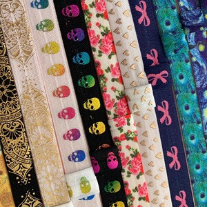 May include: A collection of colorful elastic hair ties with various patterns, including sunflowers, paisley, skulls, hearts, bows, and a starry night sky.