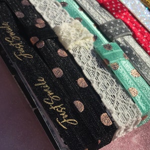 May include: A set of hair ties with various patterns, including polka dots, lace, and glitter. The hair ties are black, white, grey, red, and green. The hair ties have gold lettering that says "Just Breathe".