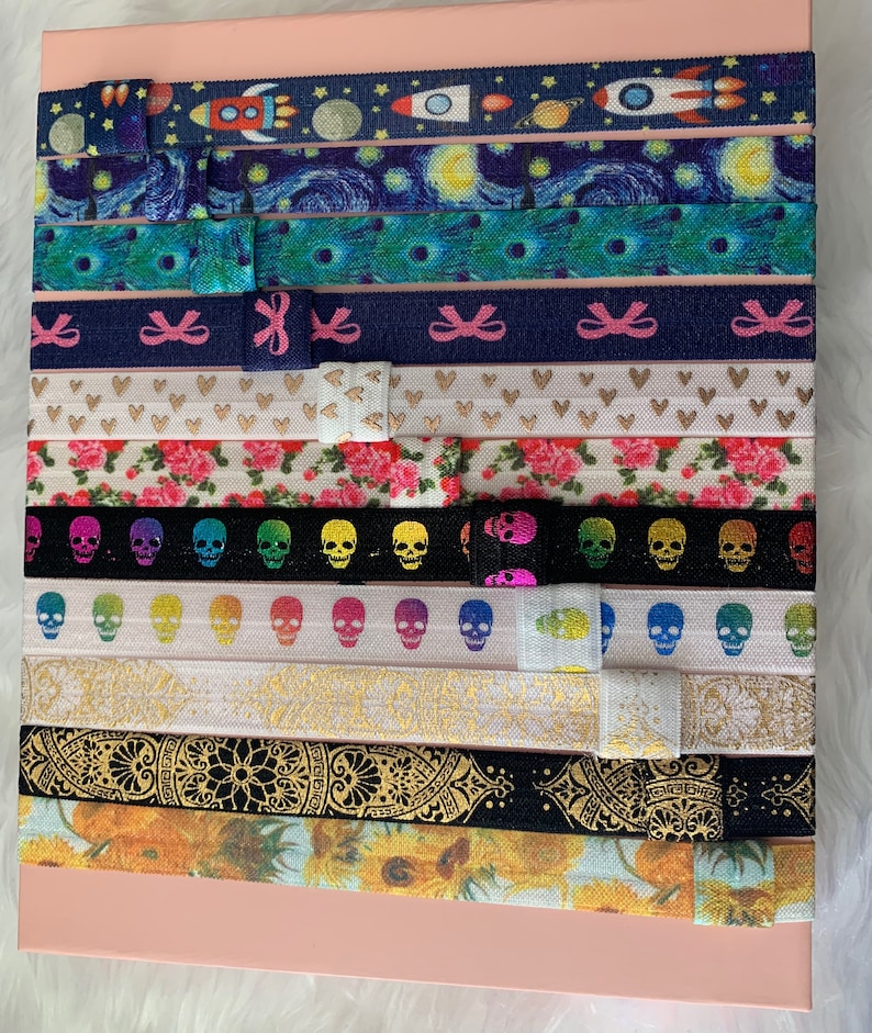 May include: A set of 12 colorful hair ties with various patterns, including a starry night sky, skulls, flowers, and geometric designs.