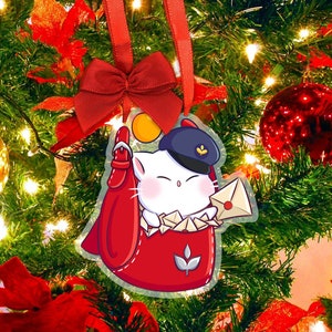 Könnte beinhalten: Ein Weihnachtsbaumschmuck mit einer Cartoon-Katze in Postbotenuniform. Die Katze mit blauem Hut hält einen Brief. Der rot-weiße Schmuck hängt an einem roten Band und einer Schleife vor einem geschmückten Weihnachtsbaum.