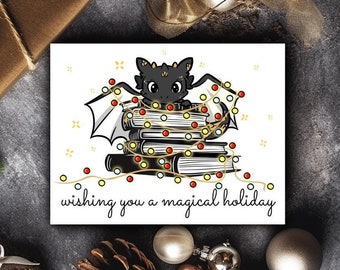 May include: A black and white illustration of a dragon curled up in a stack of books with Christmas lights wrapped around them. The text "Wishing you a magical holiday" is below the image.