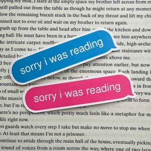 K&ouml;nnte beinhalten: Zwei blaue und rosa Aufkleber mit dem Text "sorry i was reading" darauf. Die Aufkleber sind auf einem Buch mit Text platziert.