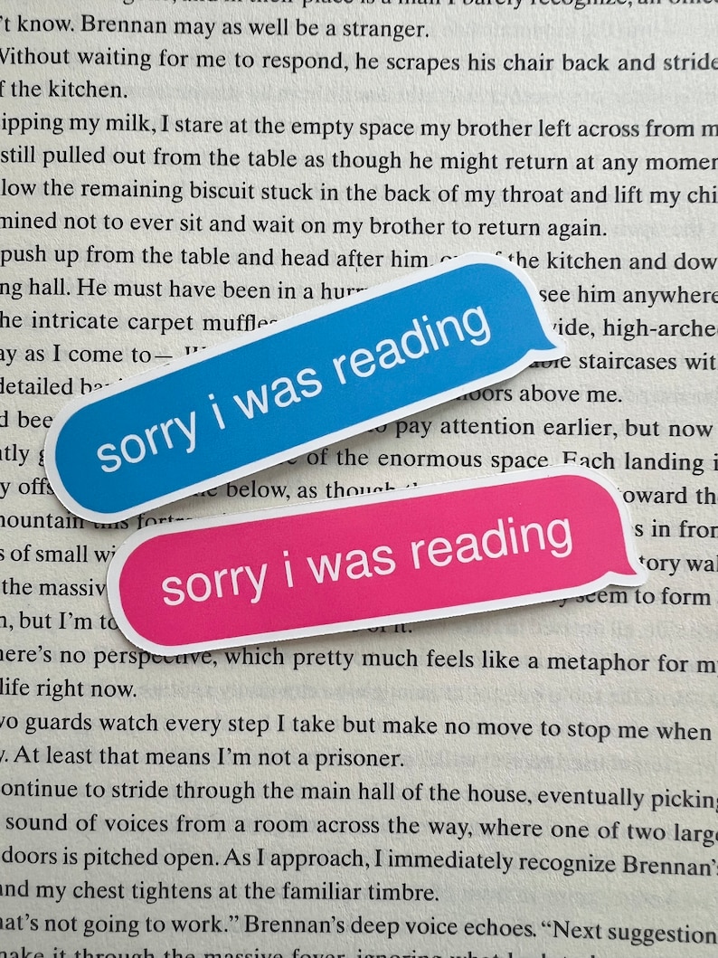 K&ouml;nnte beinhalten: Zwei blaue und rosa Aufkleber mit dem Text "sorry i was reading" darauf. Die Aufkleber sind auf einem Buch mit Text platziert.
