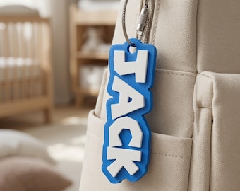 May include: A blue and white 3D printed name tag featuring the name JACK in bold white letters on a blue background. The tag is attached to a beige fabric backpack with a silver metal wire loop and a screw-top fastener mechanism.
