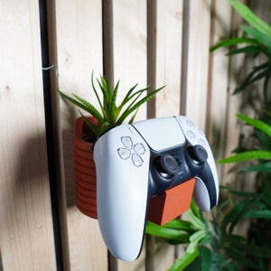 May include: A white and black video game controller mounted on a wall with a small potted plant next to it.