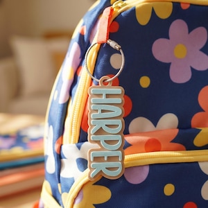 Personalized kids keychain "Harper" in tan and teal — 3D printed custom backpack charm clipped to a navy floral back to school backpack zipper