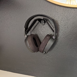 Puede incluir: Auriculares negros con diadema y almohadillas negras colgados en una pared negra.