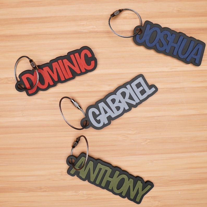 May include: Four keychains with different names on them. The names are Joshua, Dominic, Gabriel, and Anthony. The keychains are made of a soft, flexible material and have a black metal ring.