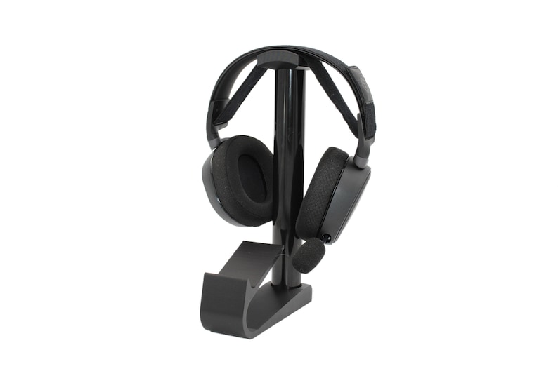 May include: Black headphone stand with a black headset resting on it. The stand has a curved base and a vertical post.