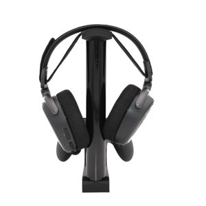 May include: A black headset stand with a black headset hanging on it. The stand has a round base and a tall, cylindrical post.