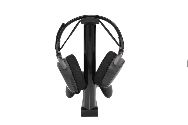 May include: A black headset stand with a black headset hanging on it. The stand has a round base and a tall, cylindrical post.