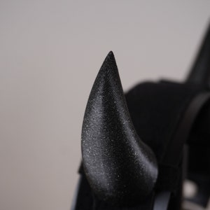 Op de afbeelding: Een close-up van een zwart, glitterend duivelshoorn haarband. De hoorn is puntig en heeft een textuur.