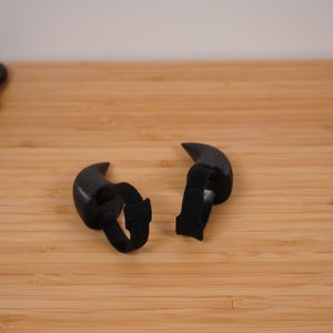 Op de afbeelding: Twee zwarte plastic hoorns met zwarte elastische banden om aan een hoofd te bevestigen.