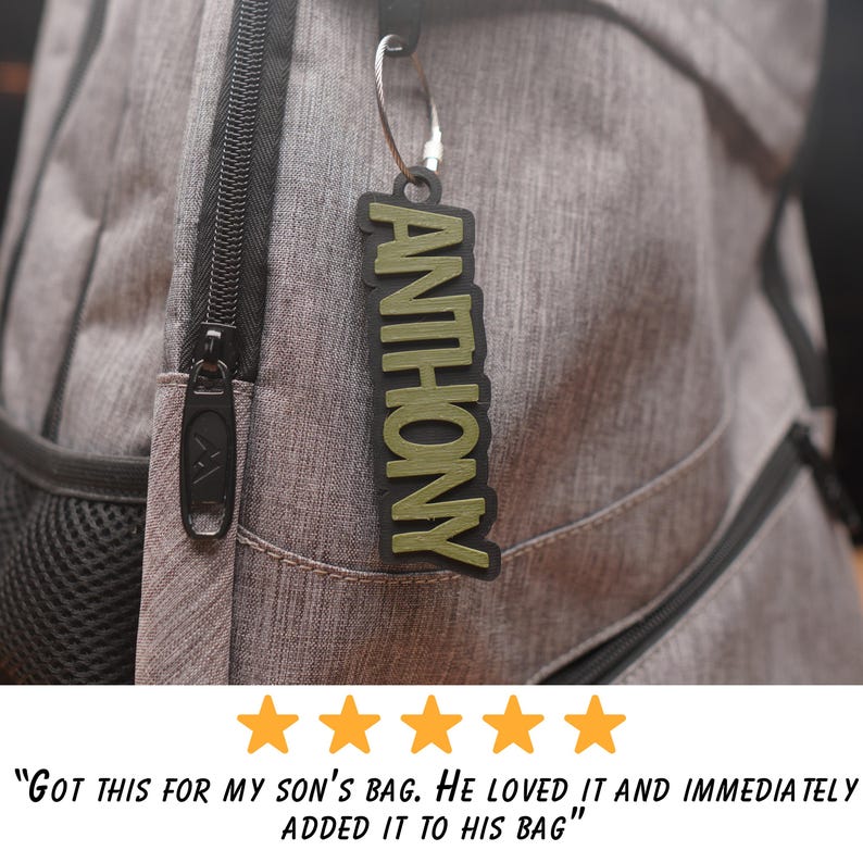 May include: A green and black personalized name tag with the name "ANTHONY" printed on it. The tag is attached to a silver key chain and is hanging from a gray backpack.