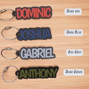 May include: Four personalized keychains with names DOMINIC, JOSHUA, GABRIEL, and ANTHONY in different colors. The keychains are dark red, dark blue, ash grey, and dark green.