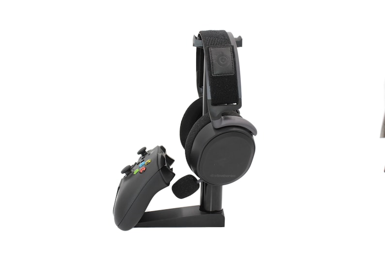 May include: A black gaming headset with a microphone and a black controller stand on a white background.