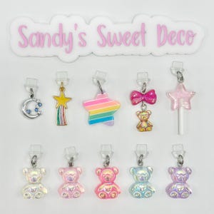 May include: Assortment of 10 colorful charms featuring a rainbow star, a star with a rainbow stripe, a pink bow with a teddy bear, a pink star lollipop, a silver crescent moon with blue stars, a yellow star with a rainbow stripe, and 5 iridescent teddy bears in different colors.