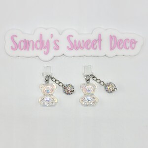 May include: Two iridescent white teddy bear charms with silver chains and iridescent crystal ball accents.  The charms are attached to clear plastic clips.  The text "Sandy's Sweet Deco" is visible in the background.