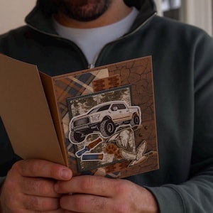 May include: A handmade greeting card featuring a layered design with a white pickup truck illustration, two flying ducks, and shotgun shell graphics. The background includes a brown cracked texture, plaid patterns, and forest imagery.