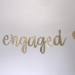 May include: Gold glitter banner with the word "engaged" and two hearts.