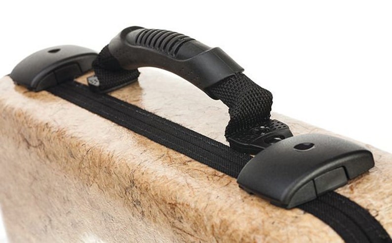 May include: A tan-colored case with a black zipper and a black handle. The handle is made of a textured rubber material and has a black strap.