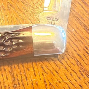 May include: A folding pocket knife with a dark brown, textured handle and a polished silver metal bolster. The blade is partially visible and features the stamped text CASE XX U.S.A. near the base, showing a metallic finish and sharp edge.