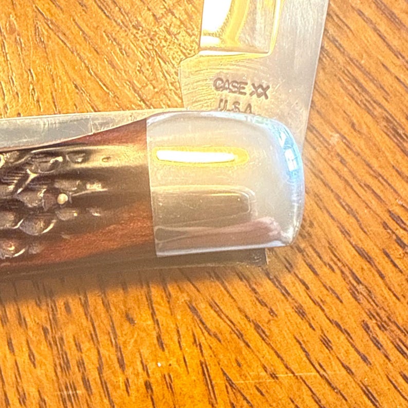 May include: A folding pocket knife with a dark brown, textured handle and a polished silver metal bolster. The blade is partially visible and features the stamped text CASE XX U.S.A. near the base, showing a metallic finish and sharp edge.