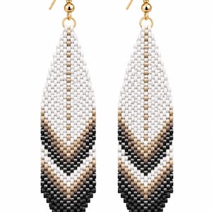 May include: A pair of long, leaf-shaped dangle earrings crafted from small seed beads. The design features a vertical gradient pattern transitioning from white at the top to metallic gold, then brown, and finally black at the pointed bottom edge.
