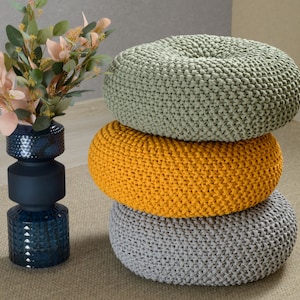 May include: Three round knitted poufs stacked on top of each other. The top pouf is light green, the middle pouf is yellow, and the bottom pouf is gray.