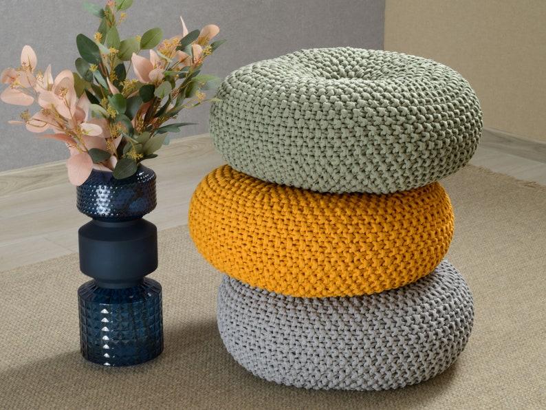 May include: Three round knitted poufs stacked on top of each other. The top pouf is light green, the middle pouf is yellow, and the bottom pouf is gray.