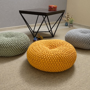 May include: Three round knitted floor cushions in different colors. The cushions are light green, yellow, and gray. The cushions are on a light brown rug.