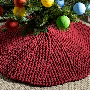 May include: A red knitted Christmas tree skirt with a textured, puffy design. The skirt is round and has a diameter of approximately 122 cm.
