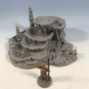 May include: A gray 3D printed miniature of a coral reef with a small figure standing on a base. The reef has multiple levels and is designed for tabletop gaming.