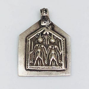 May include: A silver pendant with a detailed design of two figures standing side-by-side within a rectangular frame.