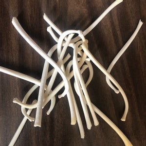 May include: A collection of off-white, curved, and straight pieces, possibly bone or a similar material, scattered on a dark brown wooden surface. The pieces vary in length and thickness, with some appearing broken or cut.