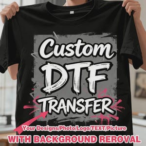 May include: A black t-shirt featuring a central gray square graphic with white brush-style text that reads Custom DTF TRANSFER. Below the graphic, pink text reads Your Designs/Photo/Logo/TEXT/Picture WITH BACKGROUND REMOVAL.