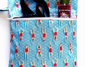 Peut inclure: Une pochette en tissu carrée avec un fond bleu clair ornée d'un motif répétitif de nageurs en maillot de bain rouge sur des vagues bleues. La pochette possède une fermeture éclair blanche et contient une sangle sombre et un flacon Yves Rocher.