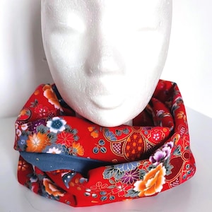 May include: A red infinity scarf with a floral pattern in orange, white, and purple. The scarf is wrapped around a white mannequin head. The inside of the scarf is a solid blue fabric.