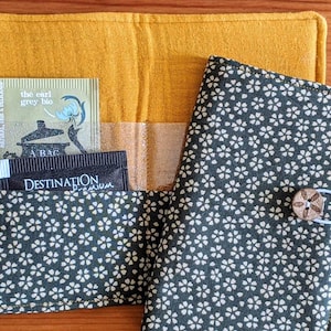 Peut inclure: Un étui à thé fait main avec un extérieur jaune moutarde et un intérieur à motifs. L'étui contient des sachets de thé, dont Clipper Earl Grey Bio et Destination Premium. Un bouton en bois et une boucle élastique ferment l'étui.
