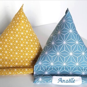 May include: Two triangular fabric phone stands. One is yellow with a white floral pattern, the other is blue with a white geometric design. The blue stand has the name "Ana&euml;lle" embroidered on a white label.