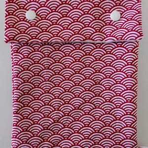 May include: A rectangular fabric pouch featuring a repeating red and white wave pattern. The pouch has a fold-over flap secured by two white plastic snap buttons. A small white fabric tag is visible at the bottom right corner of the pouch.