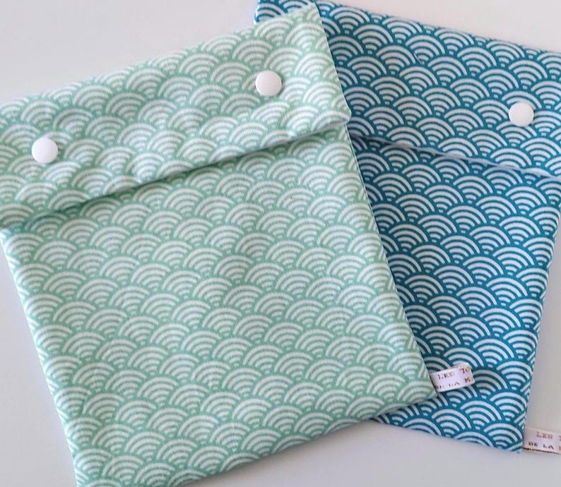 May include: Two fabric pouches with a repeating white wave pattern. One pouch is light mint green and the other is teal blue. Each pouch features a fold-over flap secured by two white plastic snap buttons and a small white fabric tag on the side.