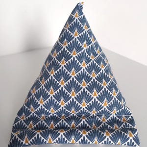 May include: A pyramid-shaped fabric tablet stand featuring a repeating pattern of blue fan-like shapes and small yellow triangles on a white background. The base includes two horizontal stitched ridges designed to hold a device in place.