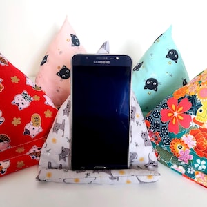 Peut inclure: Un smartphone est placé dans un support de téléphone en tissu, entouré de quatre autres supports. Les supports présentent des motifs colorés d'inspiration japonaise avec des motifs de chats en rouge, rose, blanc, turquoise et des motifs floraux. L'écran du téléphone est noir.